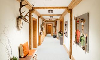 A bright hallway with wooden paneling and a cozy bench. Pictures and decorative antlers hang on the walls.