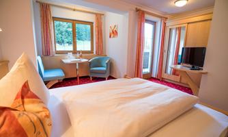 A cozy hotel room with a large bed and modern amenities. There is a small dining area, a television, and a balcony with a view of nature.