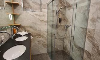 A modern bathroom with marbled walls and a glass shower cabin. Two sinks with an elegant wooden vanity and warm lighting.