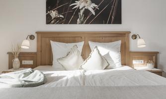 A cozy bedroom with a large wooden bed and soft pillows.  
A piece of artwork featuring a flower hangs on the wall, and the room lighting creates an inviting atmosphere.