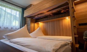A cozy bedroom with wood paneling and a comfortable bed. The window lets in plenty of daylight, creating an inviting atmosphere.