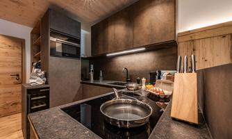 A modern kitchen with dark wood and stone surfaces. The stove is in the center, surrounded by kitchen utensils and ingredients.