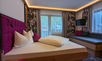 A modern room with a large bed and colorful pillows. The windows offer a view of nature, and the space has a cozy atmosphere.