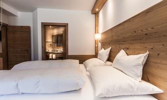 A cozy bedroom with two single beds and decorative cushions. The walls are made of wood, and the lighting creates a warm atmosphere.