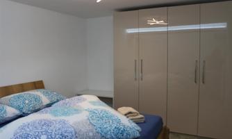 A modern bedroom with a large bed and colorful bedding. The room has a simple, bright wardrobe and pleasant lighting.