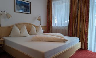 A cozy bedroom with a large bed and two pillows. The room has light curtains and a beautiful window.
