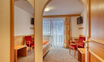 A cozy room with two red chairs, a bed, and large windows. The decor is simple and modern, with a warm hue.