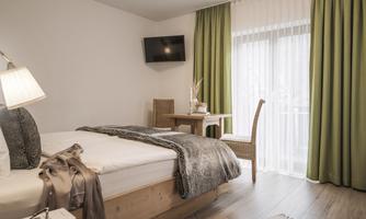 A bright and cozy bedroom with a bed and a table.  
Large windows let in plenty of light and the decor is modern and inviting.