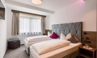 A modern hotel room with two single beds and elegant decor. Large windows let in plenty of daylight.