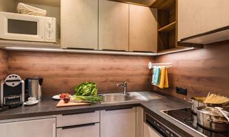 A modern kitchen with wooden paneling and black countertops. There are various kitchen appliances, fresh vegetables, and pasta-making utensils on the table.