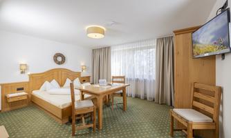 A cozy room with a double bed and a dining area. Large windows let in plenty of light and the decor is made of wood.