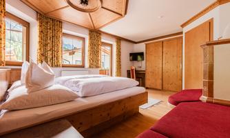 A cozy bedroom with two beds and wood-paneled walls. Bright windows provide plenty of daylight and an inviting atmosphere.