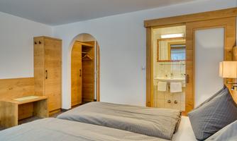 A simple room with two single beds, wooden furniture, and a bathroom. The room has a bright, inviting atmosphere.