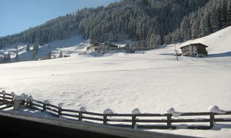 A snowy landscape with mountains in the background. In the foreground, some cottages and a fence can be seen.
