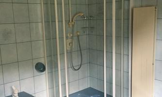 A bathroom with a blue shower cabin and a bidet. The walls are equipped with bright tiles.