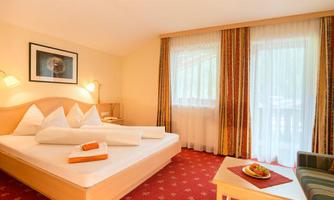 A cozy hotel room with a double bed and colorful curtains. On the table, there are fruits and a cup that enhance the inviting ambiance.