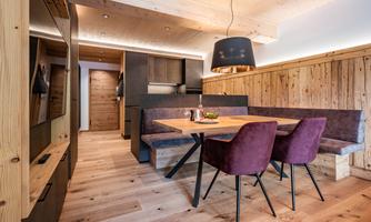 A modern, cozy kitchen with a dining table and elegant chairs. The walls are made of wood, and the lighting creates a pleasant atmosphere.