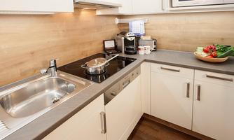 A modern kitchen with a stainless steel sink and a cooktop. Fresh vegetables and a frying pan are on the countertop.