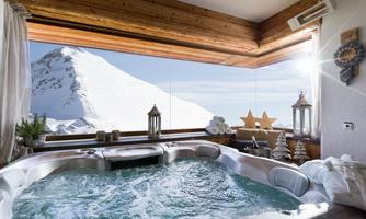 A luxurious hot tub overlooking a snow-covered mountain landscape. The light pours through the large windows, creating a relaxing atmosphere.