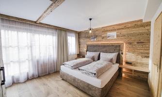 A cozy bedroom with wooden walls and a comfortable double bed. The room has large windows and a warm, inviting atmosphere.