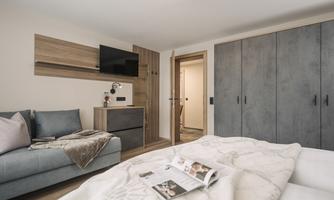 A modern bedroom with a gray sofa and a large wardrobe. A blanket is on the bed and a magazine is opened on the mattress.