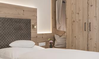 A modern bedroom with a soft headboard and a wooden wardrobe. The room is cozy and well-lit.