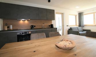 A modern kitchen with wooden and gray accents. The dining area is decorated with a large wooden table and a bowl.