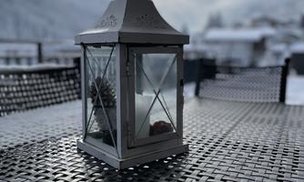 A decorative lantern stands on a table made of woven material. In the background, snow-covered landscapes and a cloudy sky can be seen.