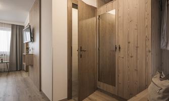 A modern entrance area with wooden cabinets and a large mirror. The walls are light, and a television is mounted on the wall.