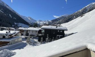 An idyllic winter scene with snow-covered hills and traditional chalets. The sky is clear and blue, completing the landscape.