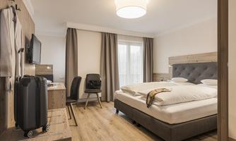 A modern hotel room with a large double bed and wooden interior. There is a desk, a television, and a suitcase in the room.