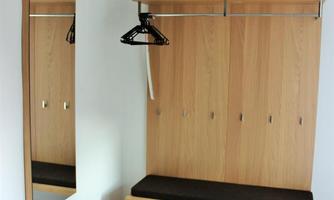 A modern hallway with a wooden cabinet and a bench. A mirror and a rug complement the furnishings.