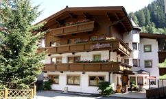A charming, traditional mountain house with several balconies and blooming flowers. Surrounded by green trees and a picturesque landscape.