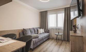 A cozy living space with a gray sofa and a small table.  
Large windows let in plenty of light, and the decorative curtains create an inviting atmosphere.