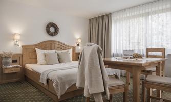 A cozy bedroom with a double bed and a dining table. Large windows provide plenty of daylight.