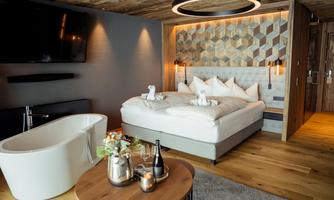 An elegant hotel room with a large bed and a modern bathtub. The warm wood tones and stylish decor create a cozy atmosphere.