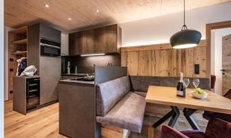 A modern kitchen with wooden details and a cozy dining area. The table is adorned with a bottle of champagne and a few snacks.