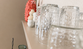 A stylish shelf with glass drinking glasses and decorative vases. In the background, colorful accents and a beautiful coaster are visible.