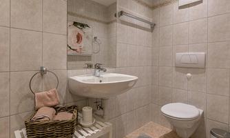 A modern bathroom with bright tiles and a sink. There are towels in a basket and a clean toilet.
