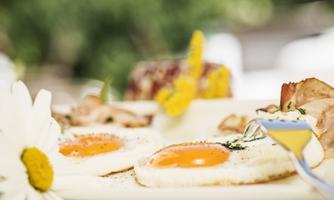 A delicious breakfast with fried eggs and fresh ingredients. On the plate, there are also some side dishes and a yellow flower.