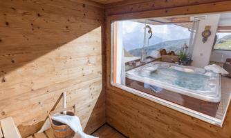 A cozy wellness area with wood paneling and a view of the mountains. In the background, a hot tub can be seen.
