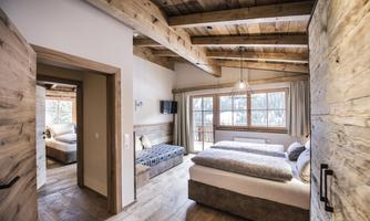 A stylish bedroom with a wooden beam ceiling and two beds. Large windows provide plenty of daylight and a view outside.