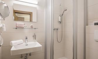 A modern bathroom with a shower and a sink. The walls are tiled in light colors and there is a large mirror.