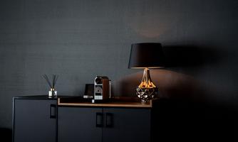 A modern sideboard in dark colors with an elegant lamp and a coffee maker. The desk lamp casts a warm light on the surface.
