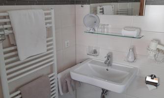 A modern bathroom with a sink, towels, and a large mirror. The walls are light-tiled and there is a heated towel rack.