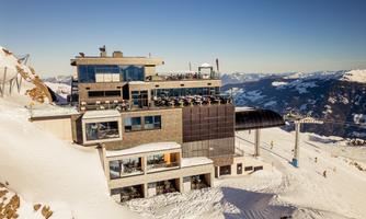 A modern mountain restaurant in the Alps, surrounded by snow-covered mountains. The view of the surrounding landscape is stunning.