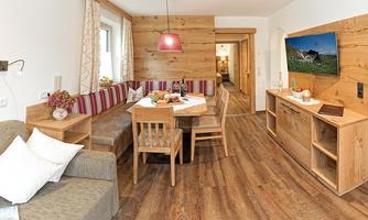 A cozy living space with wooden paneling and a round dining table. The decor is modern and inviting, featuring a sofa and a TV unit.