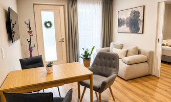 A modern living room with a dining table, two chairs, and a cozy sofa. Large window curtains and a wall mural create a pleasant atmosphere.