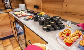 A beautifully set table with various snacks and drinks. There is fresh fruit, cold cuts, and small sweet pastries.
