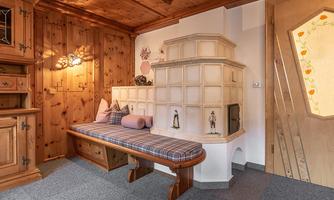 A cozy room with wooden-paneled walls and a traditional stove. A bench with cushions invites you to relax.